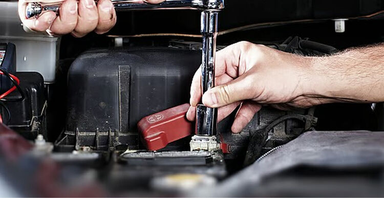 Marshall Automotive Mechanic using a ratchet on a car battery terminal in an engine bay